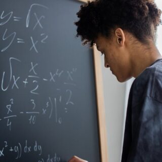 serious black student solving math equation on blackboard